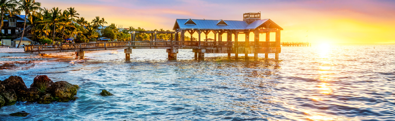 Wide shot of a pier over the ocean at sunset.