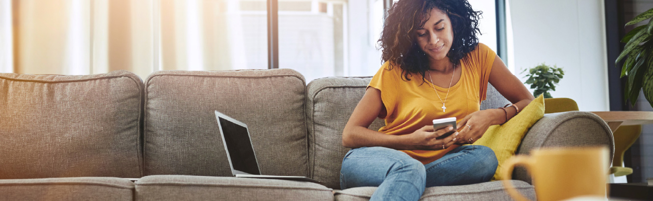 Woman sitting on a couch looking down at her phone.